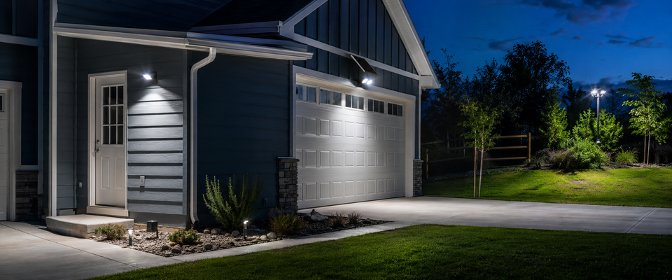 Projecteurs solaires éclairant au crépuscule une maison moderne, un garage, une allée et un jardin paysager