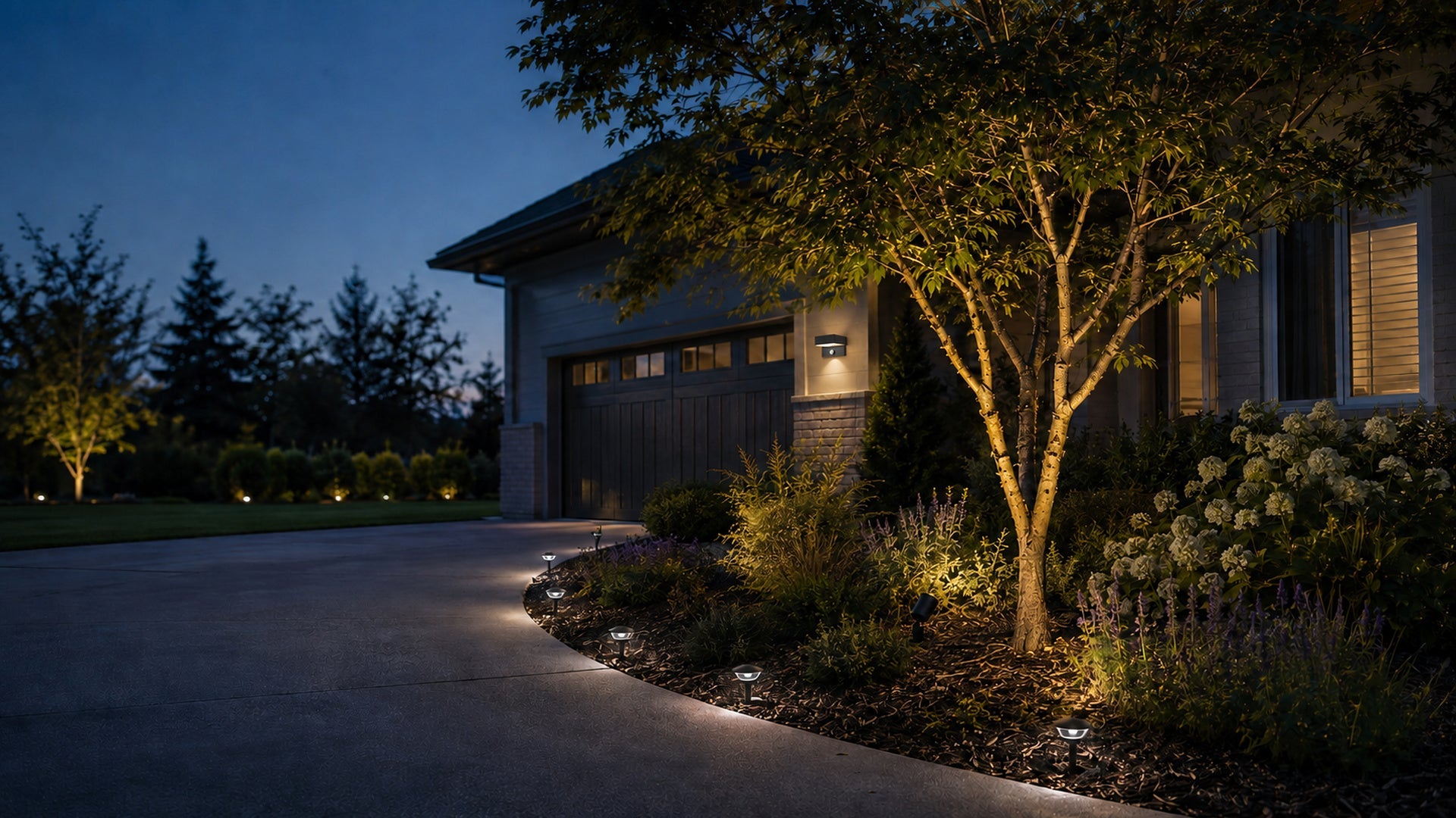 NoxLumin outdoor solar lights illuminating a residential driveway, a tree and landscaped garden at dusk