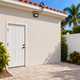Unlit 300 LED solar floodlight with separate roof-mounted panel above a Florida stucco side passage in bright late-morning daylight.