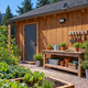 Unlit 300 LED solar floodlight above an Oregon garden potting area in afternoon daylight, with correctly scaled 23.5 by 35 cm separate solar panel secured on roof brackets.