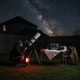Linterna de camping recargable iluminando de noche una zona de observación de estrellas junto a un telescopio