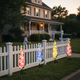 Solar delphinium flower lights glowing beside a white garden fence at night