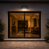 Applique solaire LED noire installée au-dessus d’une porte coulissante vitrée, éclairant l’entrée et le jardin environnant la nuit