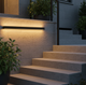 Aplique LED exterior largo iluminando de noche los escalones de entrada de una casa adosada