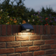 Luces solares para cercas montadas en un muro de jardín de ladrillo rojo con iluminación exterior blanca cálida y RGB