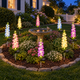 Solar delphinium flower stake lights arranged around a circular garden bed and stone birdbath outside a New England cottage at dusk.