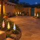 Solar delphinium flower lights in separate gravel garden beds around a spacious Santa Fe adobe courtyard at night, with sandstone paving and a turquoise garden gate.