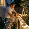 Father installing a solar LED strip light around a backyard tree and wooden fence with his children