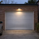 Luz solar de pared con sensor de movimiento iluminando una puerta de garaje y la entrada de vehículos por la noche