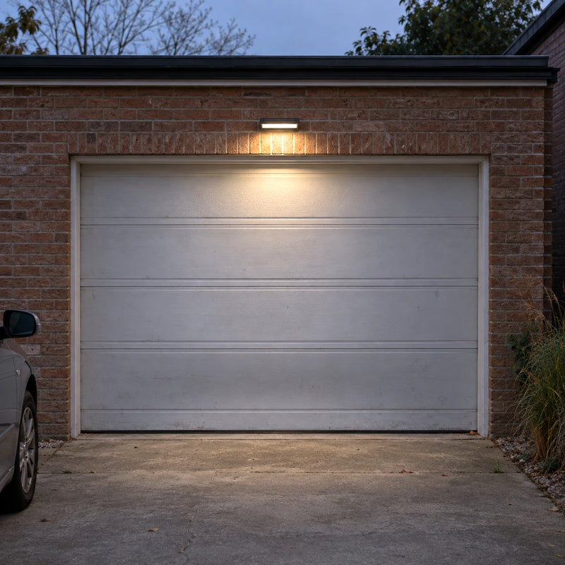 Solar motion sensor wall light illuminating a residential garage door and driveway at night