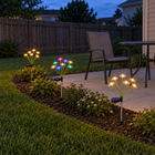 Warm white and RGB solar mushroom stake lights around a backyard patio seating area at dusk.