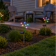 Warm white and RGB solar mushroom stake lights in a garden border beside a backyard wood deck with two Adirondack chairs.