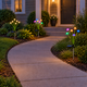 Four warm white and RGB solar mushroom stake lights arranged beside a curved front walkway at dusk.