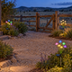 Warm white and RGB solar mushroom stake lights beside a gravel path in a Western ranch-style garden at dusk.