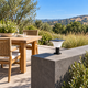 Unlit solar pillar-top light with an integrated solar panel on a concrete wall beside an outdoor dining terrace in daylight
