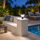 Solar pillar-top light casting cool white light on a stucco seating wall beside a pool lounge