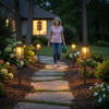 Woman walking along illuminated garden pathway at twilight